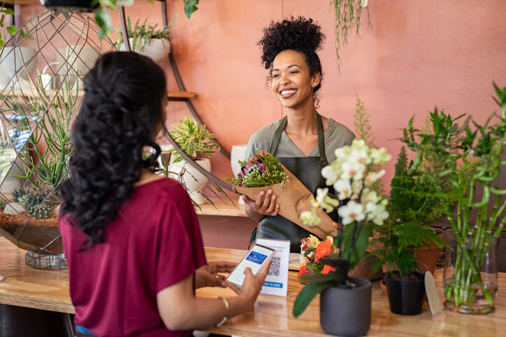 A woman smiles at a customer while holding a bouquet of flowers