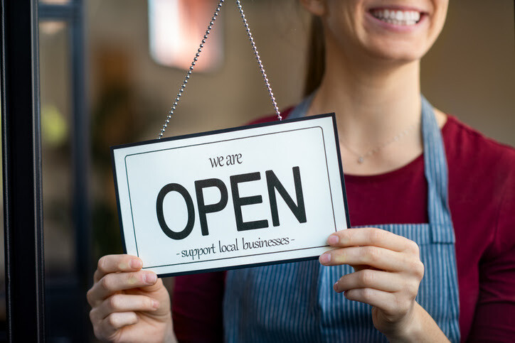 A shopkeeper smiles while holding a sign that reads, 