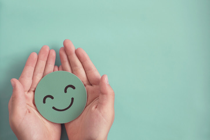 A mint green smiley face cutout is held in the palms of two hands