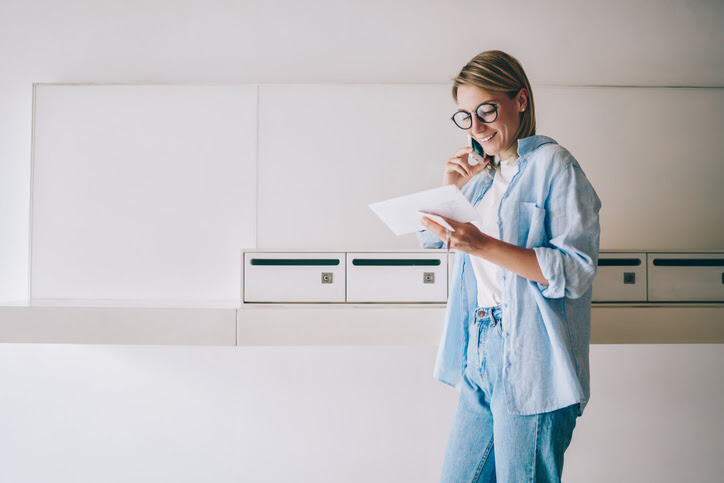 Happy woman holding an envelope and making a phone call in a bright, minimalistic space