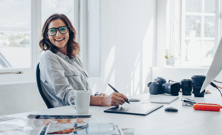 Smiling woman with glasses working on a digital tablet in a bright photography studio