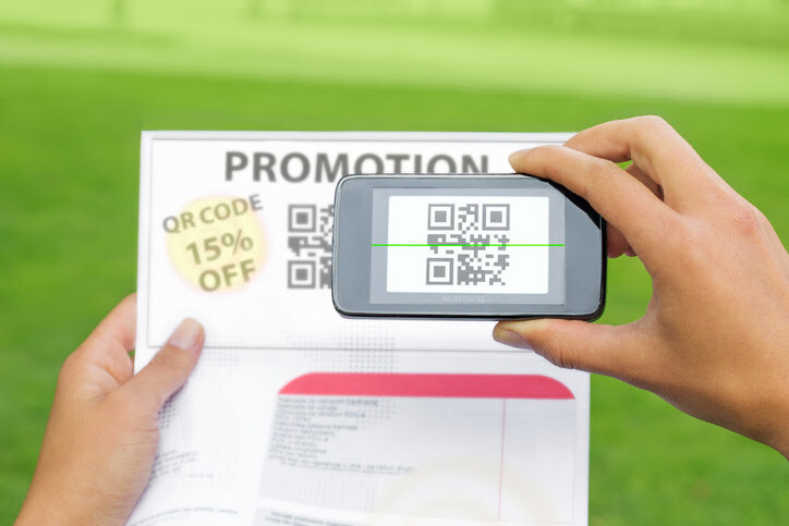 Close-up of a smartphone scanning a QR code on a printed promotion outdoors.