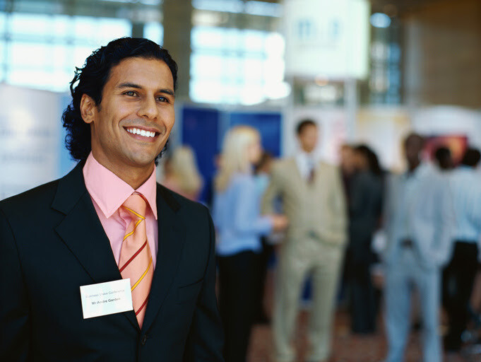 Confident professional at a business expo with attendees mingling behind him