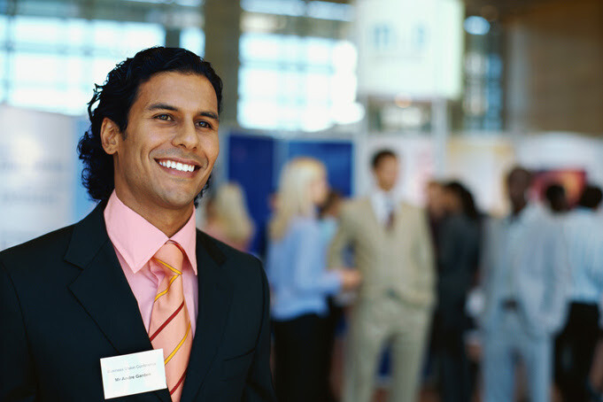 Confident professional at a business expo with attendees mingling behind him