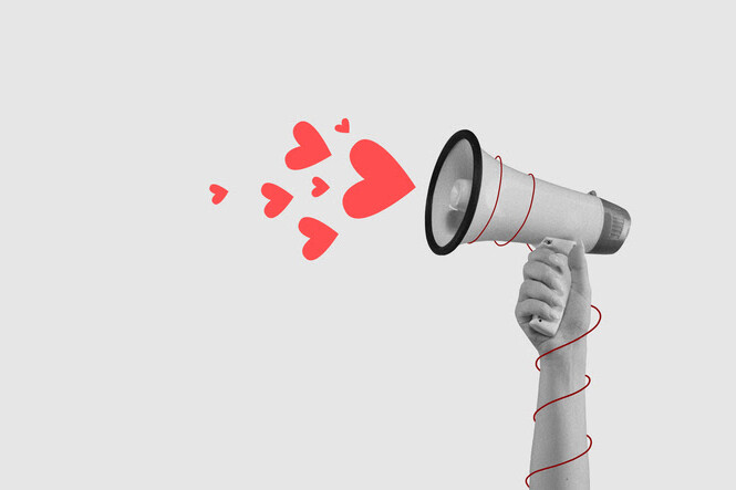 Hand holding a megaphone with red hearts coming out against a gray background.