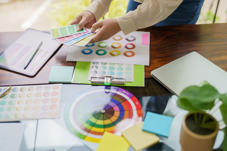 Hands organizing color samples on a desk with various design tools