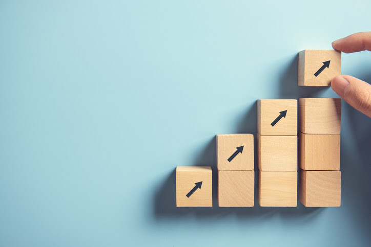 Stacked wooden cubes forming an upward trend with arrows, representing business growth