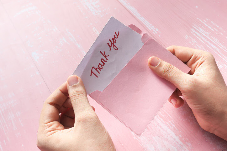 Person opening a pink envelope revealing a handwritten thank you note.
