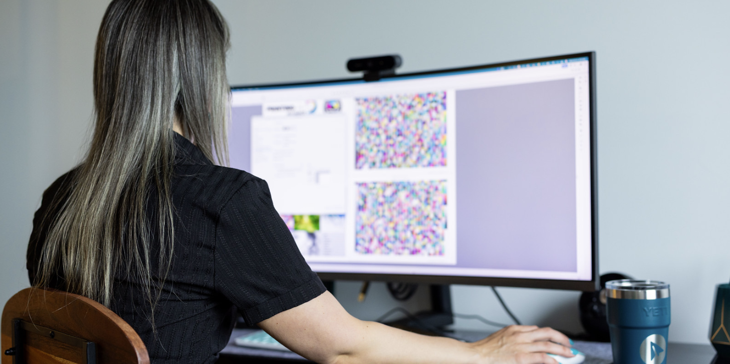 Person working at a computer, viewing colorful patterns on a large monitor.