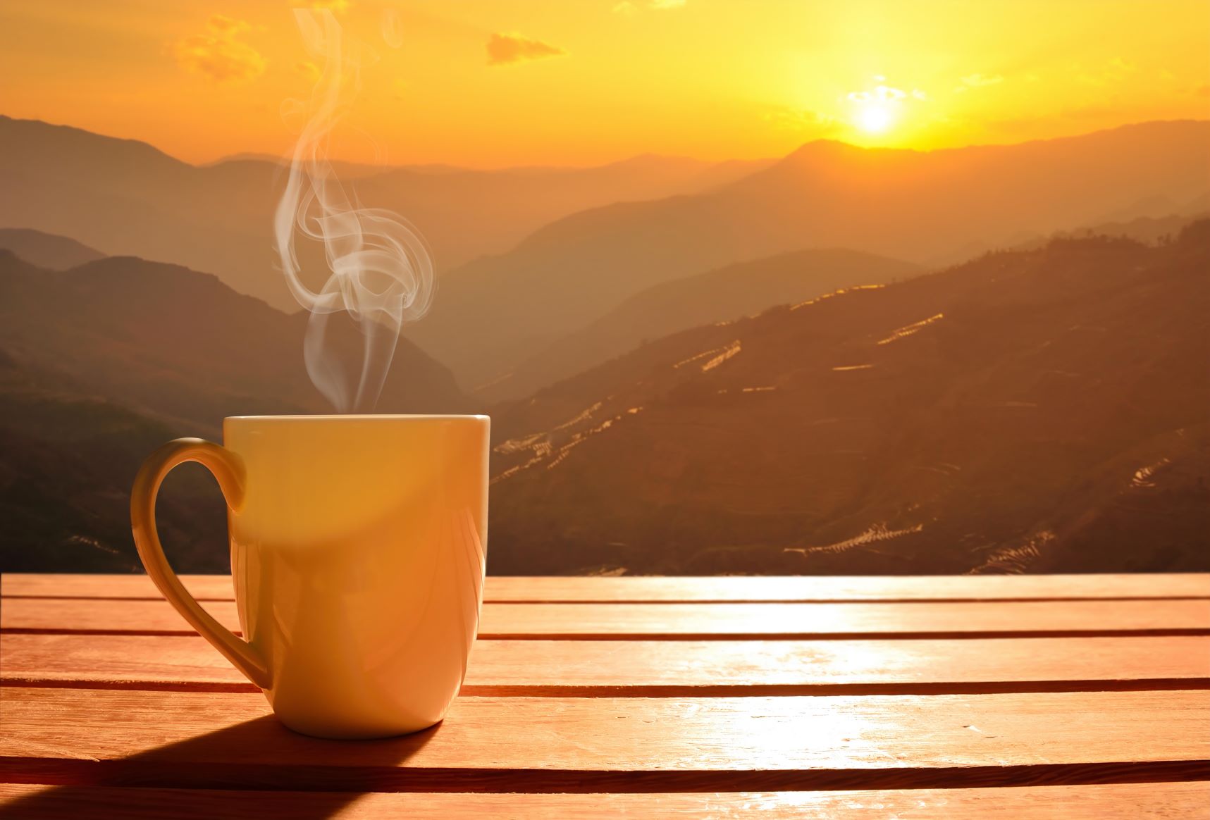 mug with steam rising out on a table with a sunrise in the background